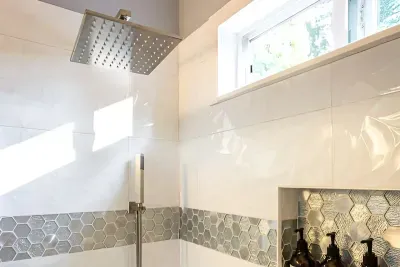 - Sleek shower with rainfall head, handheld sprayer & contemporary hardware finishes
- White textured tiles accented with metallic hexagonal band for a designer look
- Built in recessed shelf keeps bath products organized & within easy reach for use