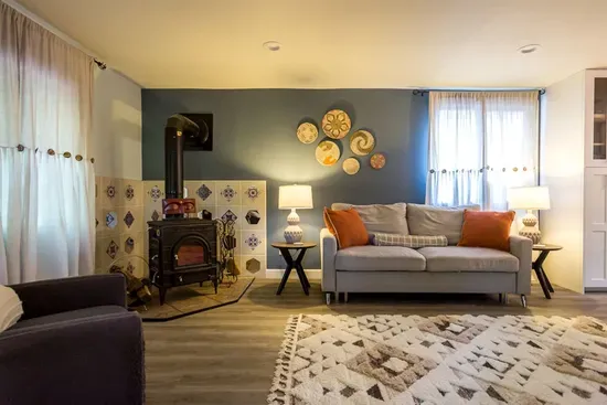 - Lounge with stylish sofa, armchair, and vibrant throw pillows for color
- Classic wood stove with decorative tile detail brings warmth & timeless character
- Layered lighting design enhances both ambiance and relaxation throughout the space