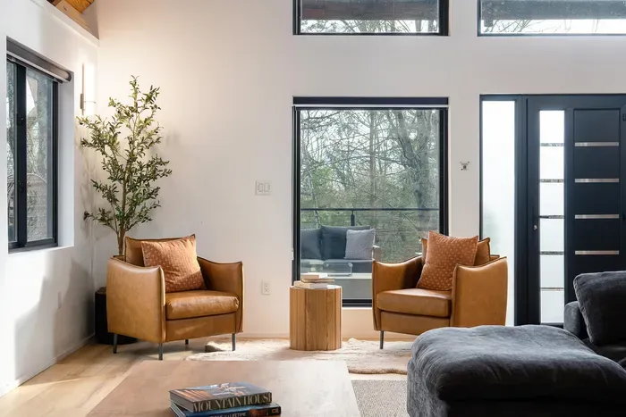 Bright modern lounge with tall windows, leather chairs, and serene wooded views