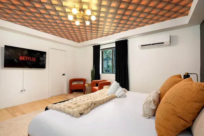 Stylish bedroom with designer ceiling, TV, AC, and cozy seating nook