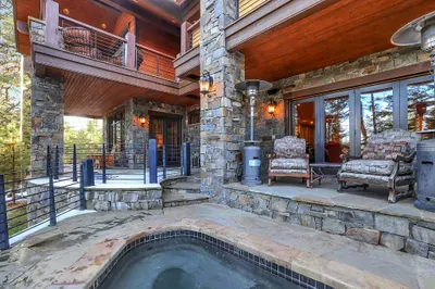 The built-in stone spa sits conveniently connects to the wraparound deck—soak under the pines, then drift back to the fire pit with a towel and a drink