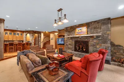 The downstairs living room is where evenings land—wood‑burning hearth, deep seating, and doors that open to the spa and fire pit