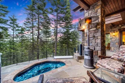 The built-in stone spa sits at tree-top level—steam rising into the pines, peaks and lake in view—turning après into an evening ritual