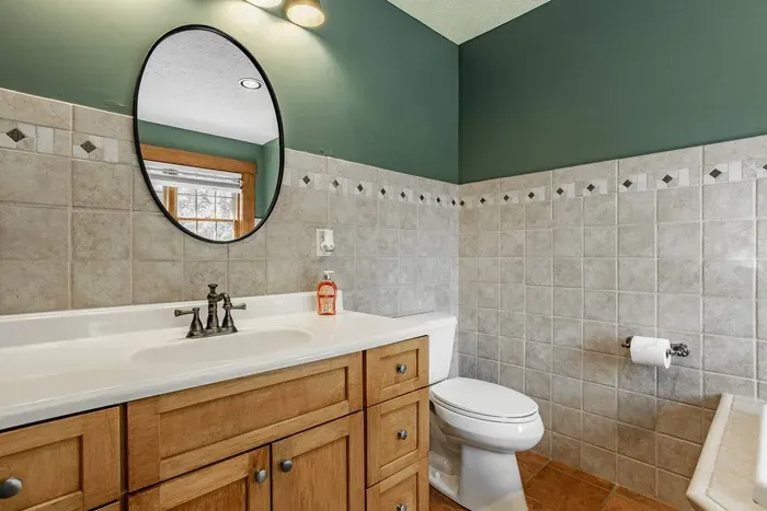 Featuring a wooden vanity with a white countertop, an oval mirror, and classic tiled walls.
