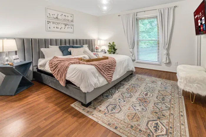 Bright airy master bedroom with king bed, plenty of pillows, a thick duvet cover, two nightstands, and a 40" Roku TV.