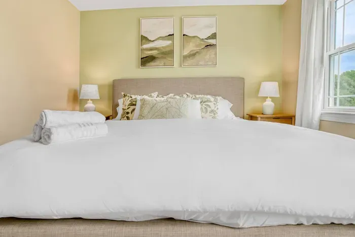Cozy bedroom with a soft neutral palette, layered pillows, and folded towels for a fresh, inviting stay.