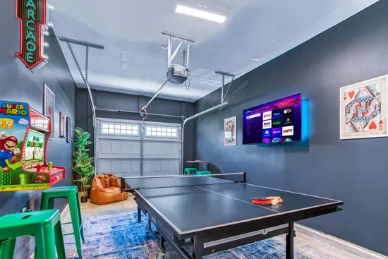 Enjoy endless fun in this vibrant game room featuring a ping pong table, retro Super Mario arcade machine, wall-mounted dartboard, and a large smart TV. 