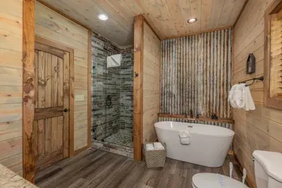 Rustic charm meets modern luxury!  Unwind in a gorgeous ensuite featuring a sleek grey tiled stand-up shower, metal tin accent wall, and a Roman tub for soaking in style.