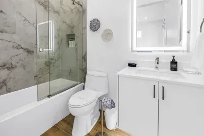Bright modern bathroom with marble-style shower and sleek lit vanity mirror