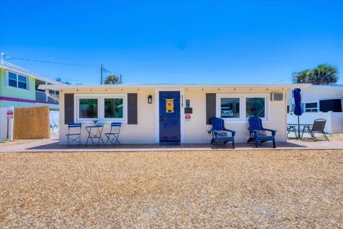 Bright beach cottage with front patio seating, navy door, coastal charm.
