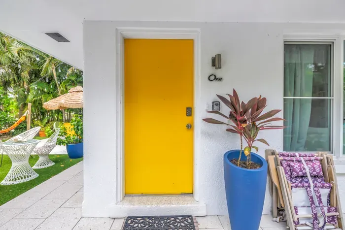 Sunny private entrance with tropical patio seating and a vibrant yellow door