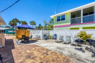 Sunny beachside courtyard with grills, loungers, and umbrella dining