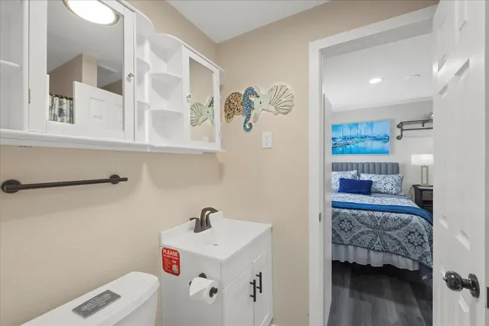 Bright coastal bath with mirrored storage, opening to a chic blue bedroom