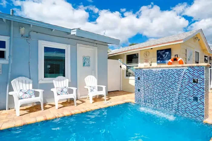 Sunny coastal patio with private pool, waterfall, and Adirondack seating.