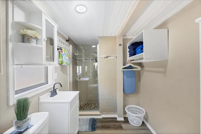 Bright bath with glass walk-in shower, modern vanity, storage & towels.