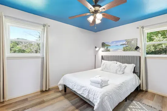 Bright bedroom with plush bed, natural light, and a stylish blue ceiling