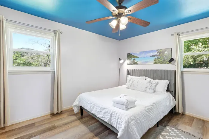 Bright bedroom with plush bed, natural light, and a stylish blue ceiling