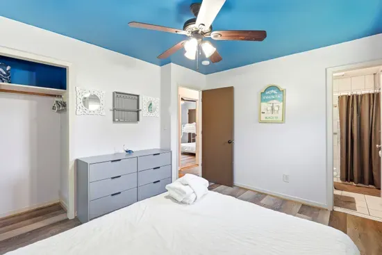 Bright coastal bedroom with bold blue ceiling and easy bathroom access