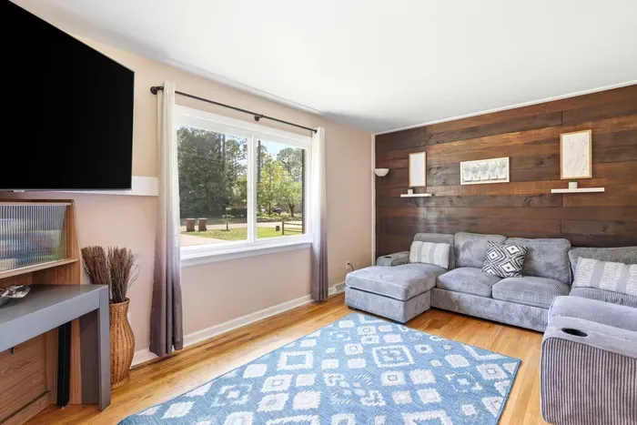 Cozy living room with sectional, wood accent wall, and sunny picture window