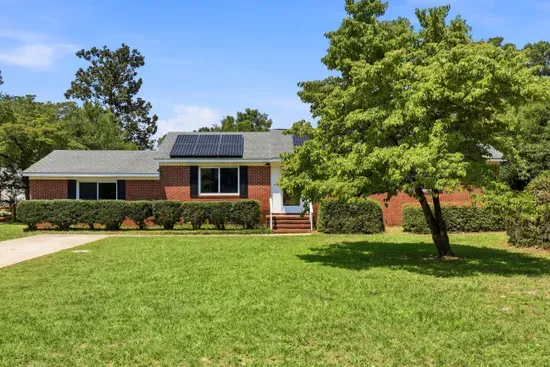 Charming brick home with spacious lawn, shade trees, and solar panels