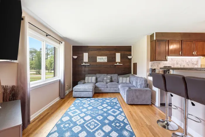 Bright living room with cozy sectional, wood accent wall, and breakfast bar