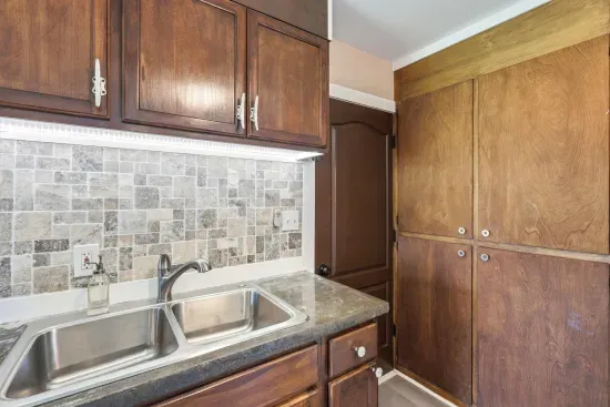 Warm kitchen with double sink, tiled backsplash, and generous storage