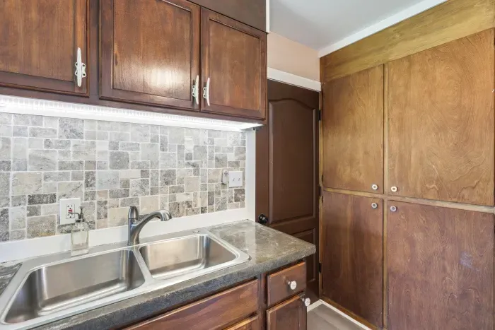 Warm kitchen with double sink, tiled backsplash, and generous storage