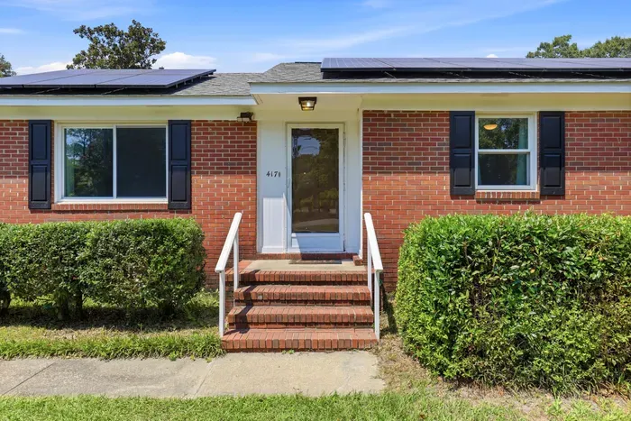 Charming brick home entry with solar panels and manicured curb appeal