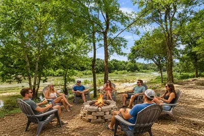 Riverside fire pit with Adirondack seating under shady trees
