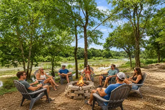 Riverside fire pit with Adirondack seating under shady trees