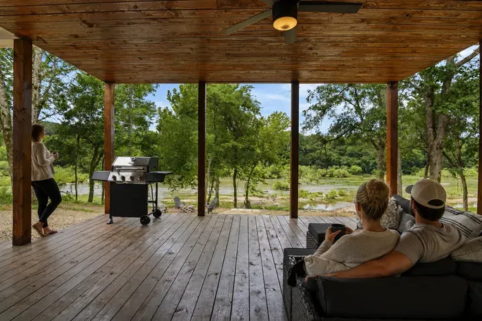 Covered riverside deck with grill, cozy seating, and serene nature views