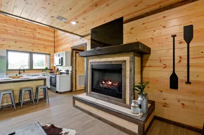 Cozy cabin living with fireplace, TV, and bright kitchen bar seating