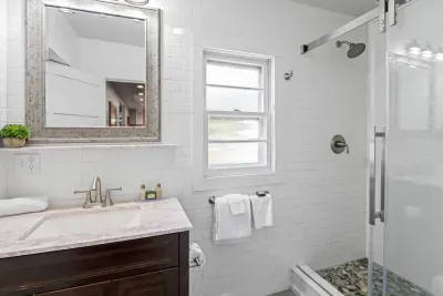 The main-level bathroom is accessible through the dining room and also the Master Bedroom. It features an updated design and sliding class-door shower with a pebble-rock flooring.