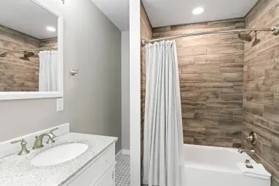 This upstairs bathroom includes a tub and shower with an updated, wood-grain wall paneling.