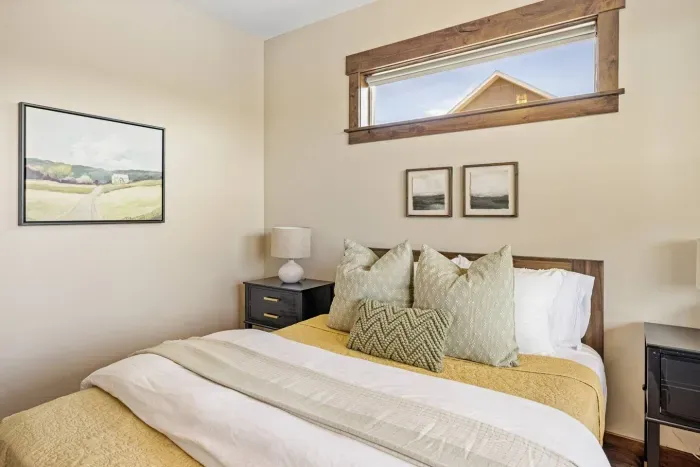 Cozy and calm, this guest bedroom features a DreamCloud mattress, soft bedding, ceiling fan, and warm natural light. The view offers a peek at open fields and Montana’s big skies at dusk.