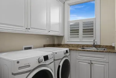 Bright laundry room with full-size washer/dryer, sink, and ample storage