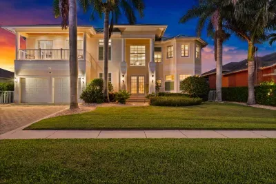 Elegant palm-lined estate with balcony, glowing entry, and grand curb appeal