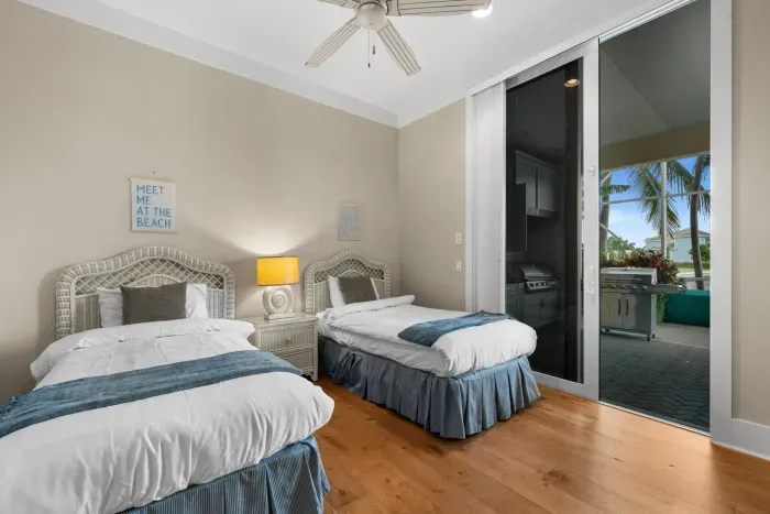 Coastal twin bedroom with patio access, tropical views, and outdoor grill
