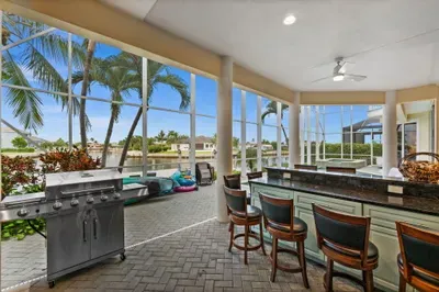 Screened waterfront lanai with outdoor kitchen, grill, and bar seating