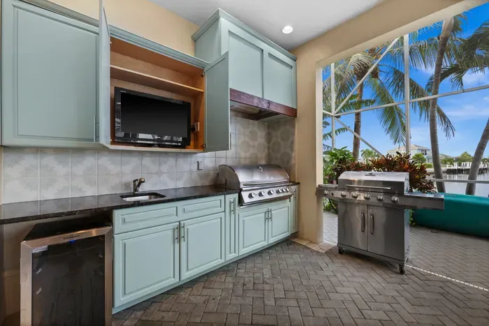 Covered waterfront outdoor kitchen with grill, TV, and tropical views