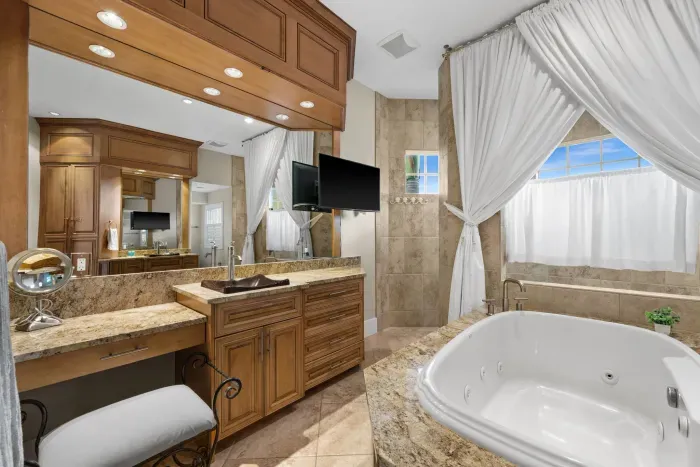 Spa-like bathroom with jetted soaking tub, granite vanity, and TV