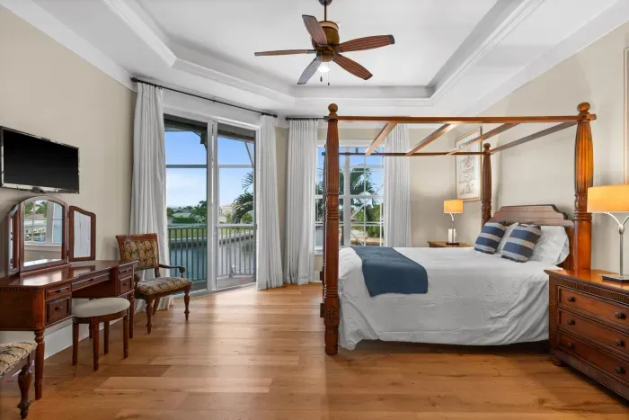 Bright waterfront king bedroom with private balcony and elegant four-poster bed