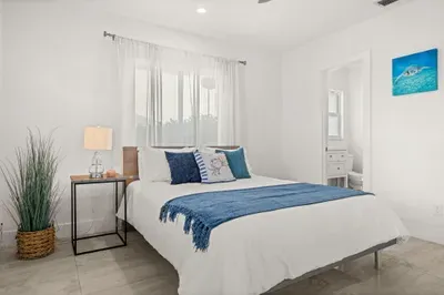 Bright coastal bedroom with queen bed and ensuite bath access