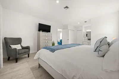 Bright coastal-style bedroom with TV, lounge chair, and en suite access
