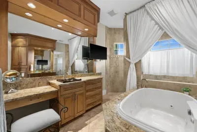 Spa-like bath with jetted tub, TV, granite vanity, and elegant drapery