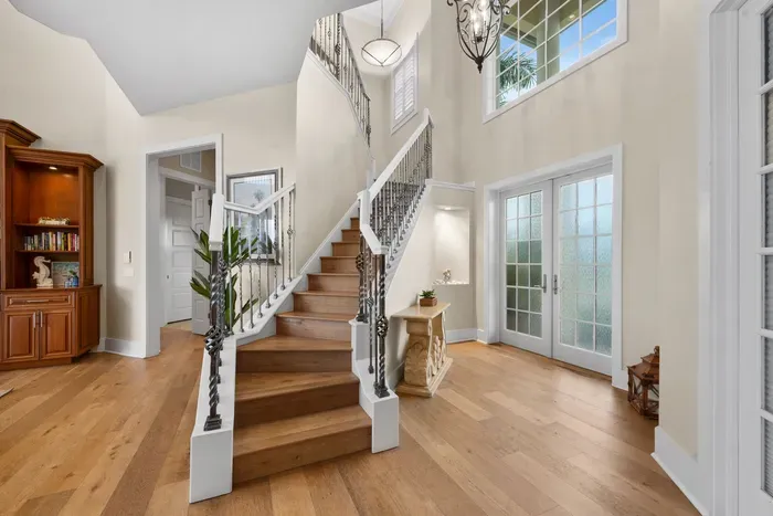 Grand sunlit foyer with elegant staircase and soaring ceilings