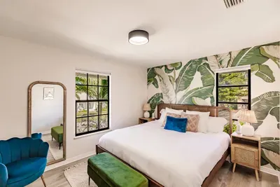 Chic Bedroom: Vibrant palm wallpaper and bright windows invite tropical vibes!