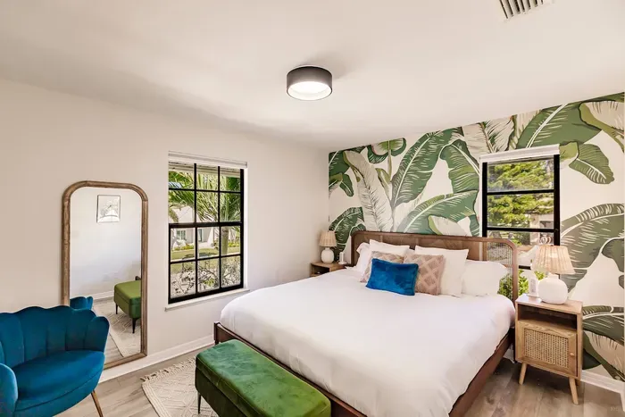 Chic Bedroom: Vibrant palm wallpaper and bright windows invite tropical vibes!