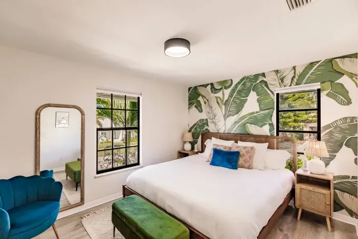 Chic Bedroom: Vibrant palm wallpaper and bright windows invite tropical vibes!