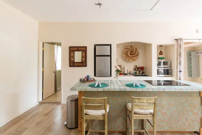 Large kitchen island with electric stovetop, sitting area, refrigerator, sink, and cooking supplies (in kitchen island)